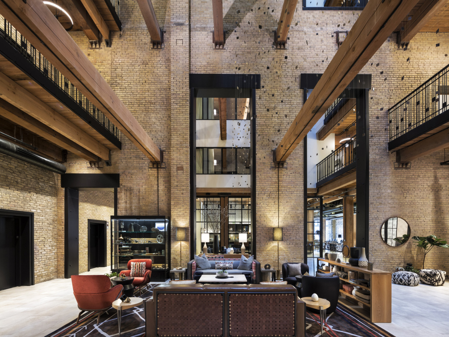 Interior atrium with exposed brick. Seating area at center and wood beams overhead. 2 walkways on sides above with metal rail, adaptive reuse hotel