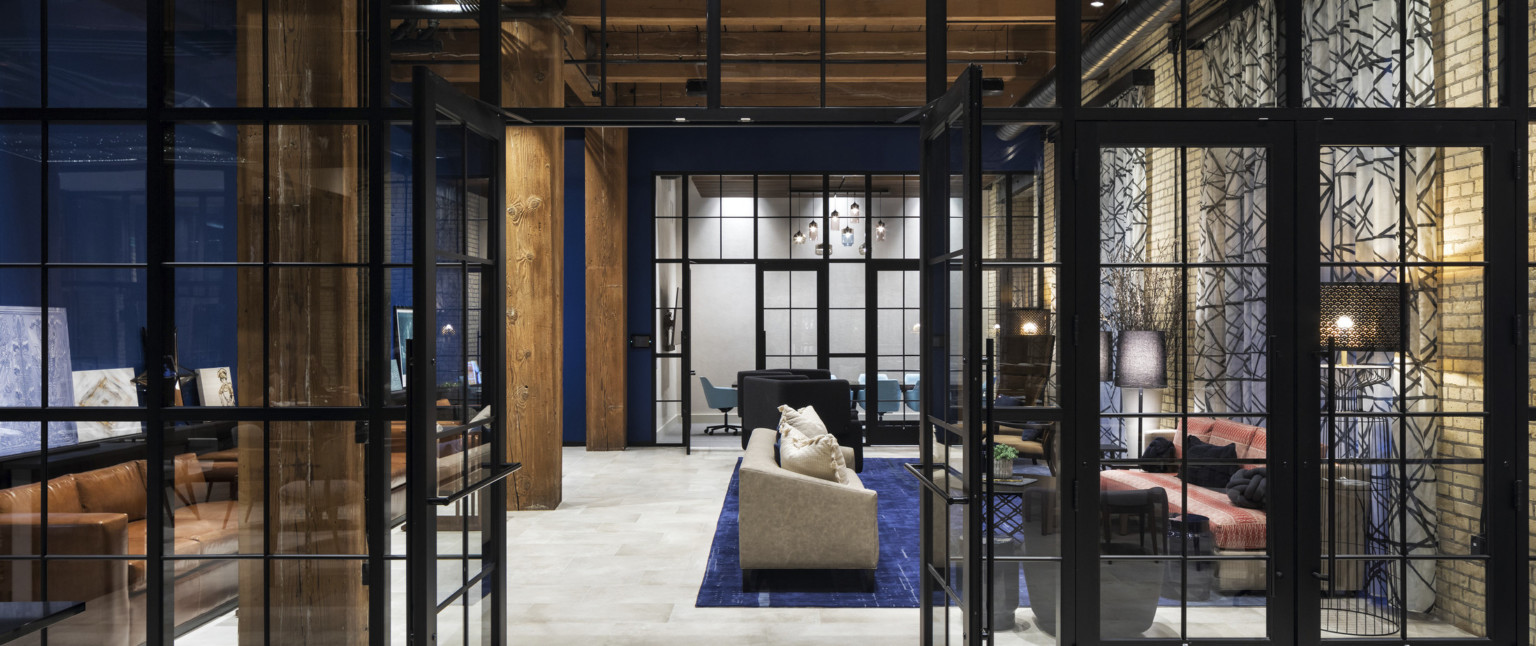 Blue room with wood columns and ceiling of sitting room with couches on blue rug. Glass wall to conference room beyond, adaptive reuse hotel