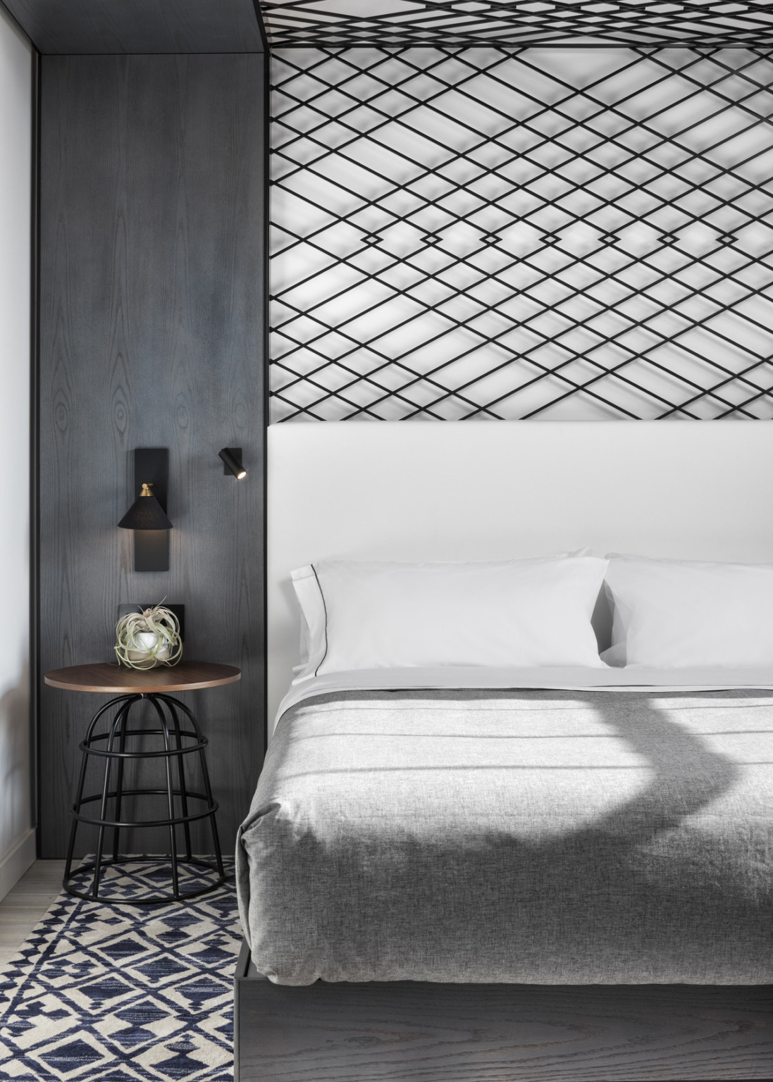 View from side foot of bed. Canopy structure behind bed and a side table with round wood top and black metal base, adaptive reuse hotel