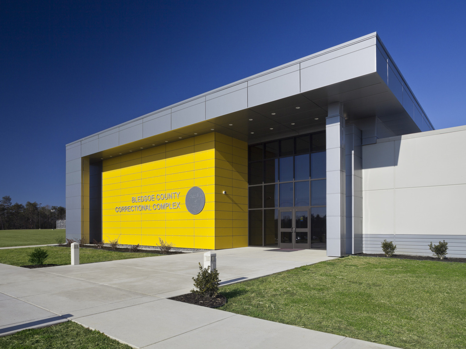 Front entry to building with yellow front wall to left of double height windows under grey overhang wrapping down side