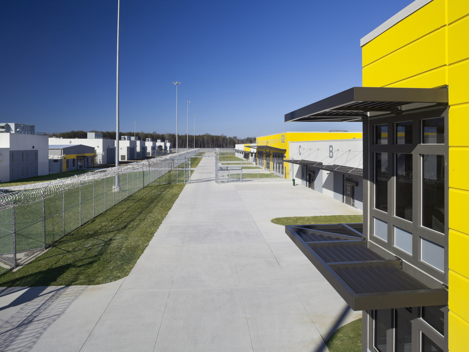 A line of alternating yellow and white buildings facing concrete walkway and tall perimeter fence