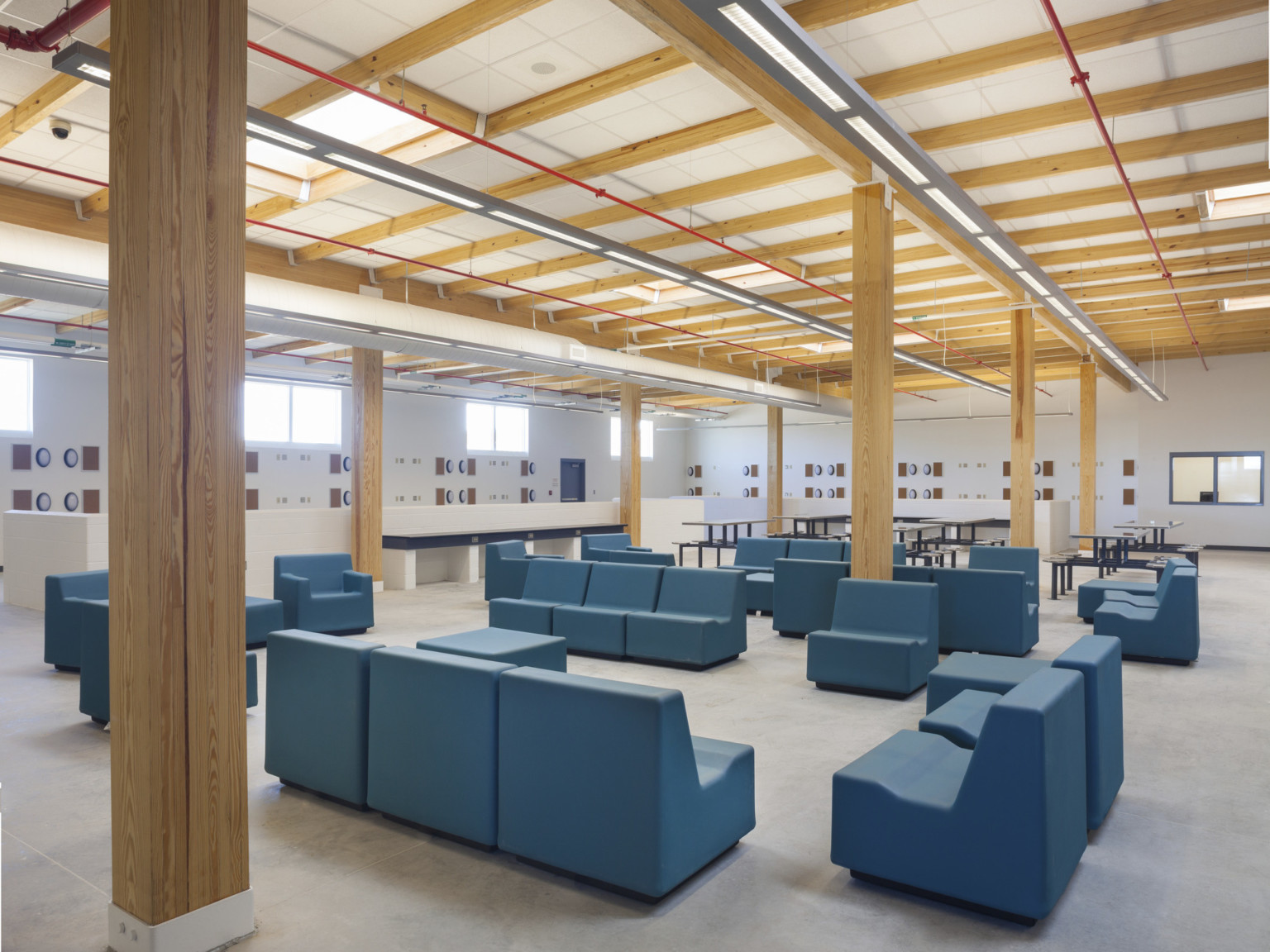 Seating area with large dark blue chairs. Wood pillars stand throughout white room with wood beams.