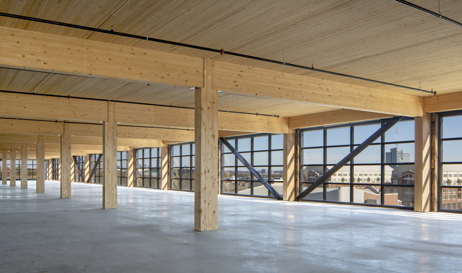 Interior with wood columns, ceiling and beams lined with floor to ceiling windows with black seams and exposed steel beams