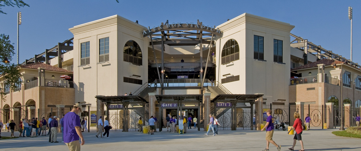 Gated entry labeled Alex Box Stadium Gate 2. Metal fence with baseball design in front of double staircase by white buildings