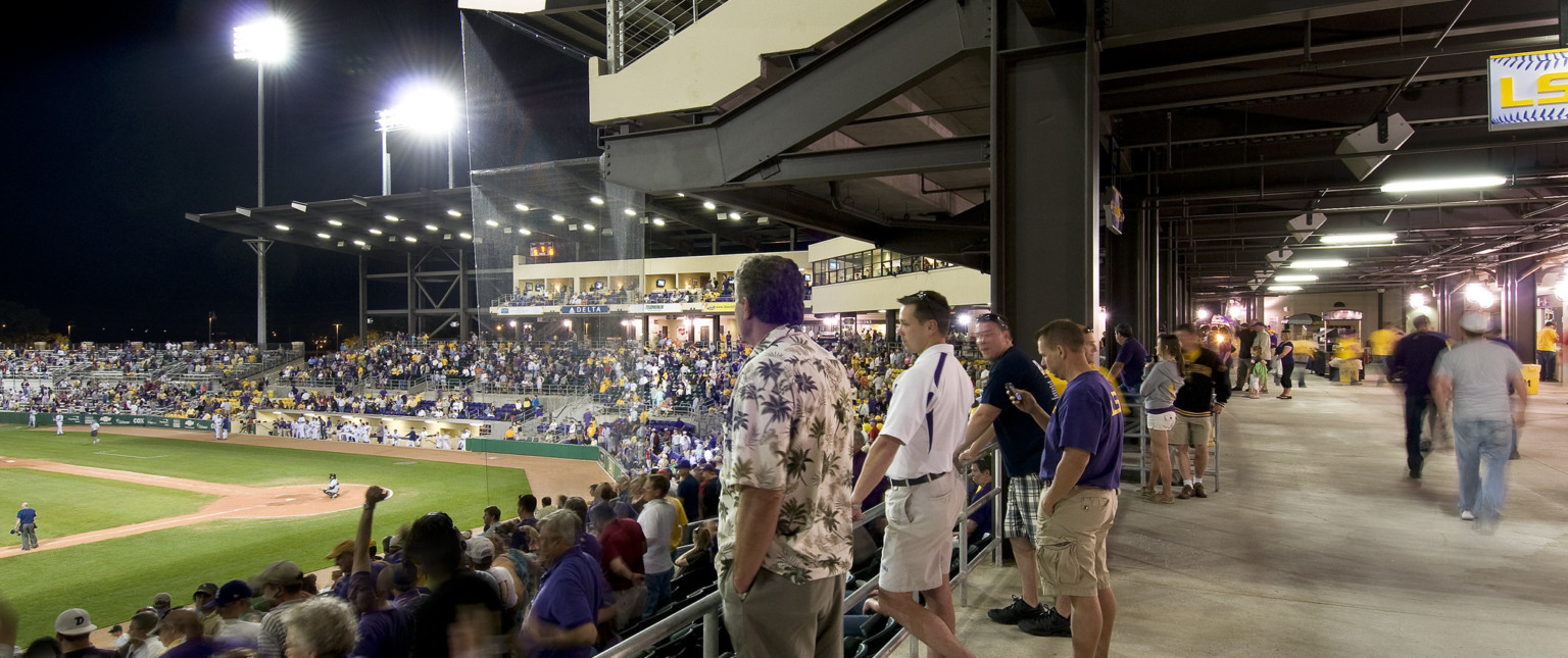 Covered walkway behind the top of lower deck seating behind home plate with box suites overhead supported by exposed beams