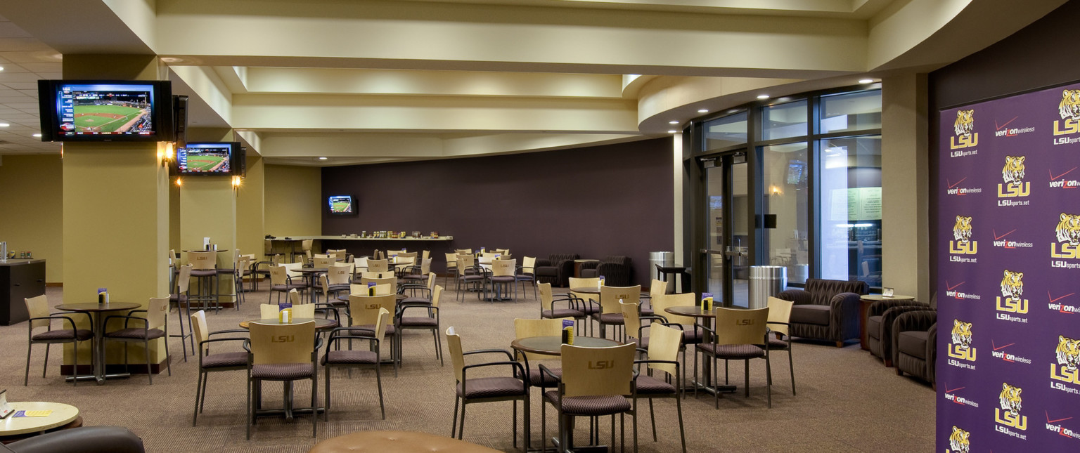 Dining area with rounded glass entry. LSU logo on chair backs in cream room. Screens on columns, purple accent wall right