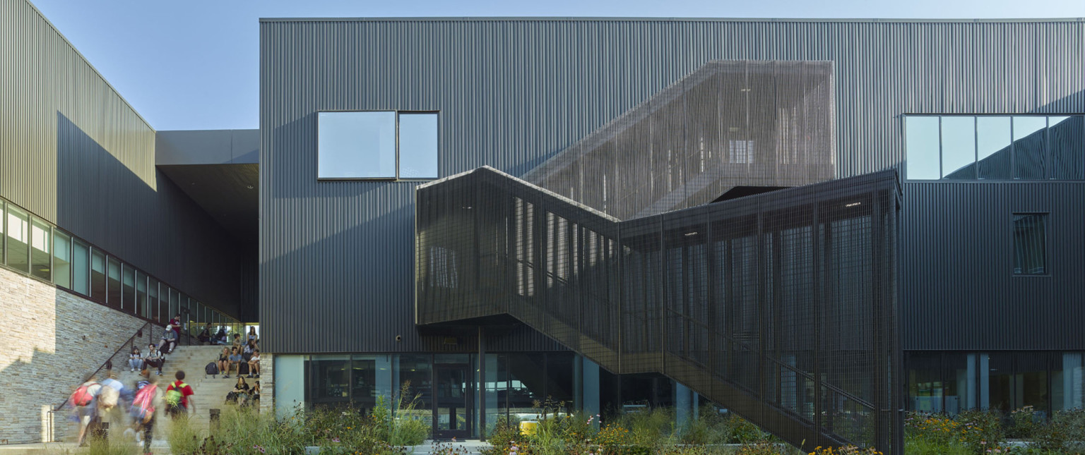 Close up view of sheltered black stairwell in courtyard with black translucent side walls. Stairs go to black panel 2nd floor