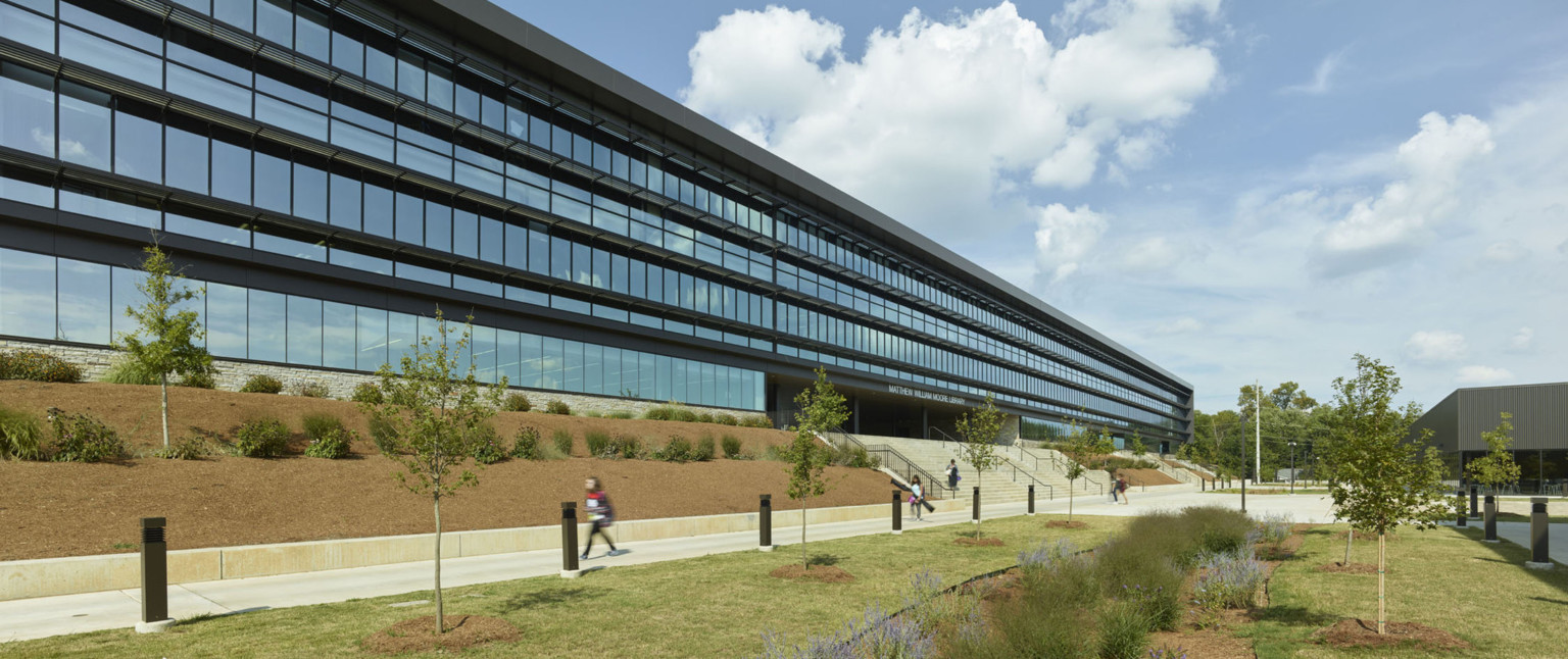 Exterior view of glass lined wall of black building with wide concrete steps leading to recessed entrance. Front, a lawn