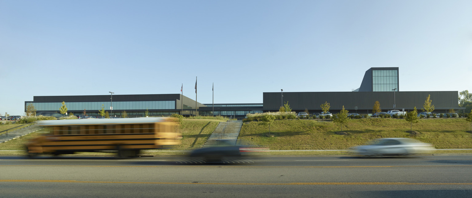 Exterior view of the school from across the street. Concrete steps are built into green hill leading up to the black building