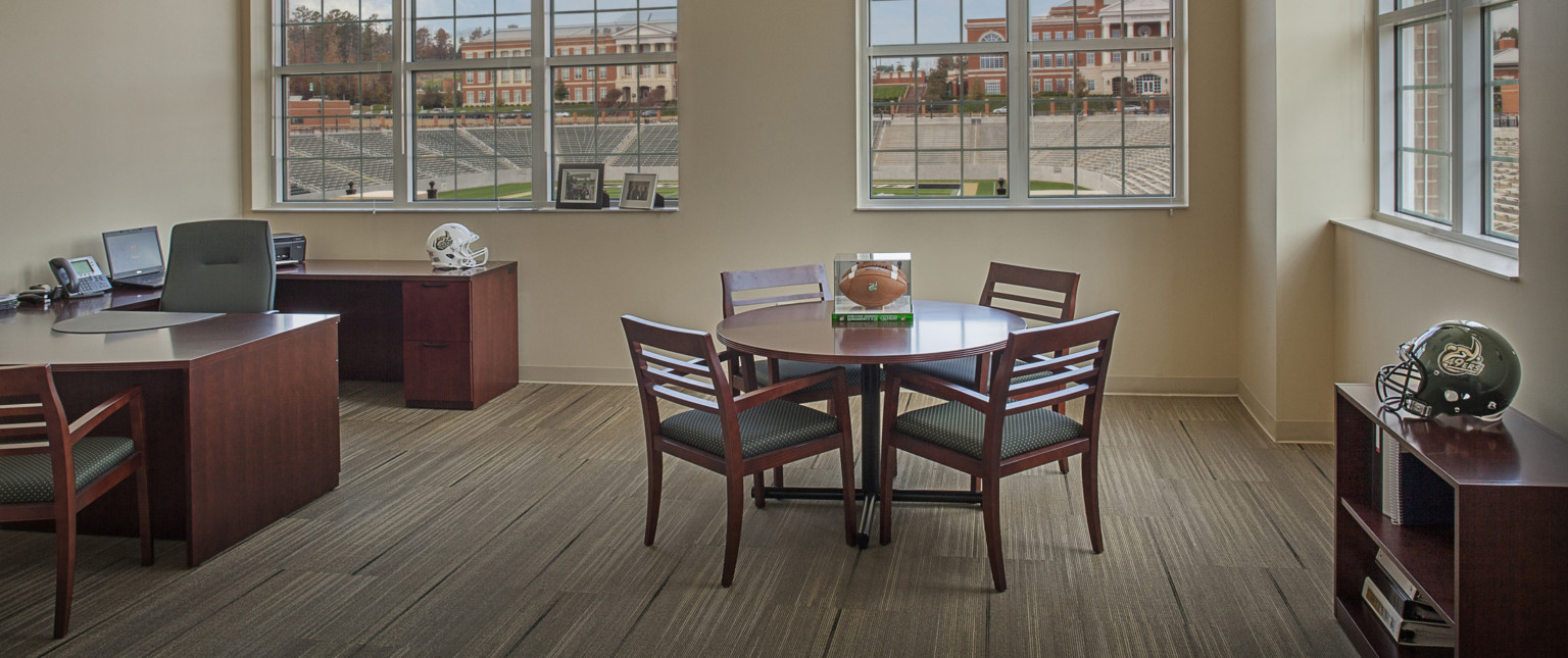 Corner office with stadium view. Horseshoe shaped wood desk in left corner with table, right, with football in display box