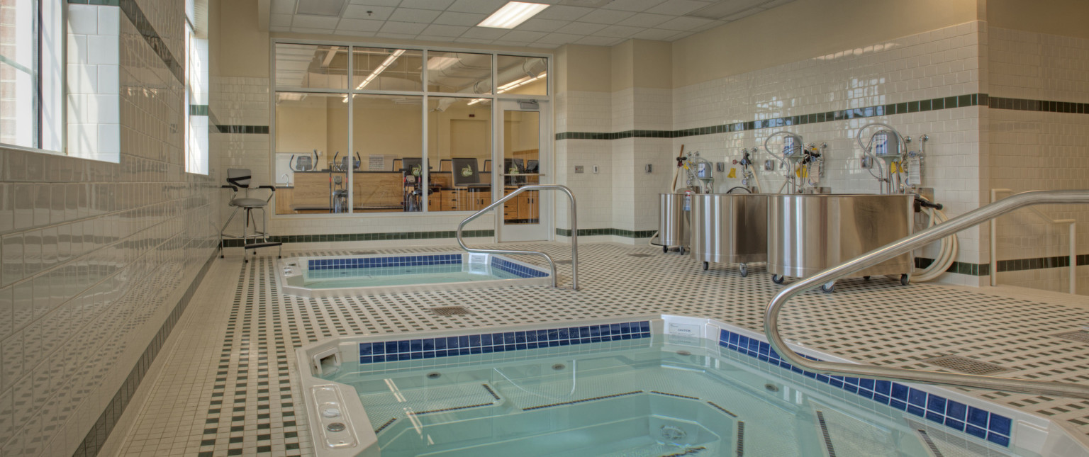 2 recovery pools in green and white tiled room with windows looking to previous room. Silver tubs along right wall