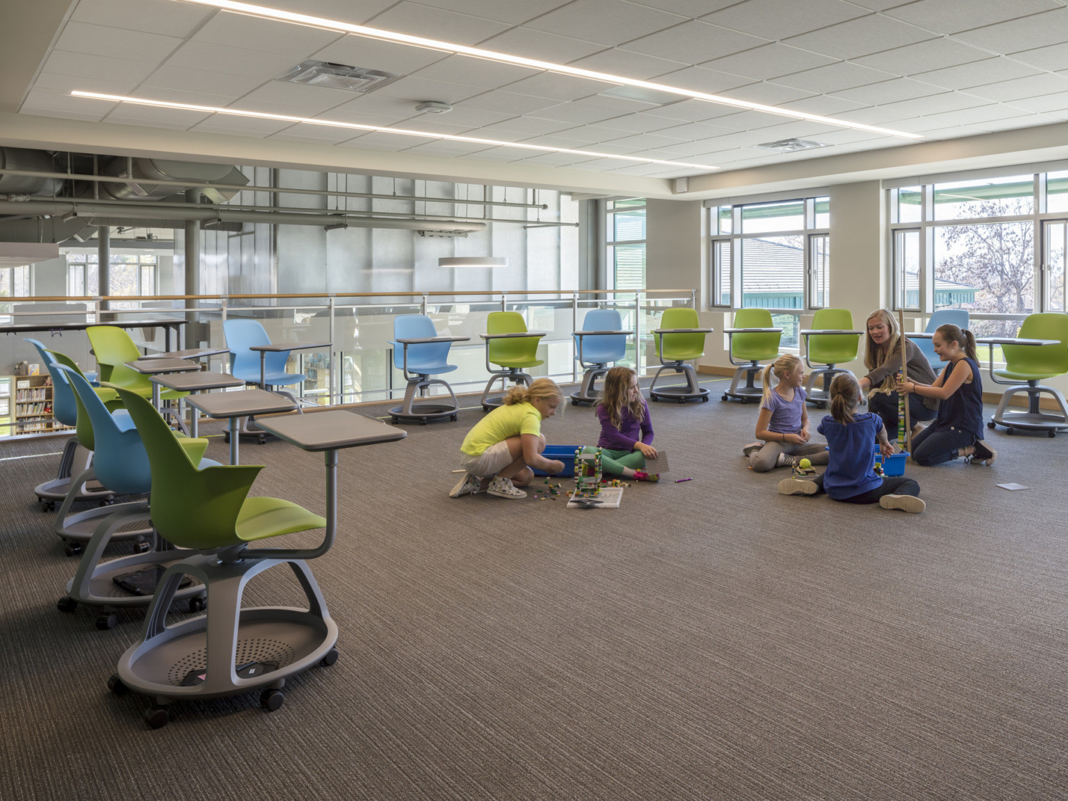 parallel lighting in acoustic tile ceiling over carpeted floor and green and blue movable kids seating with kids on floor