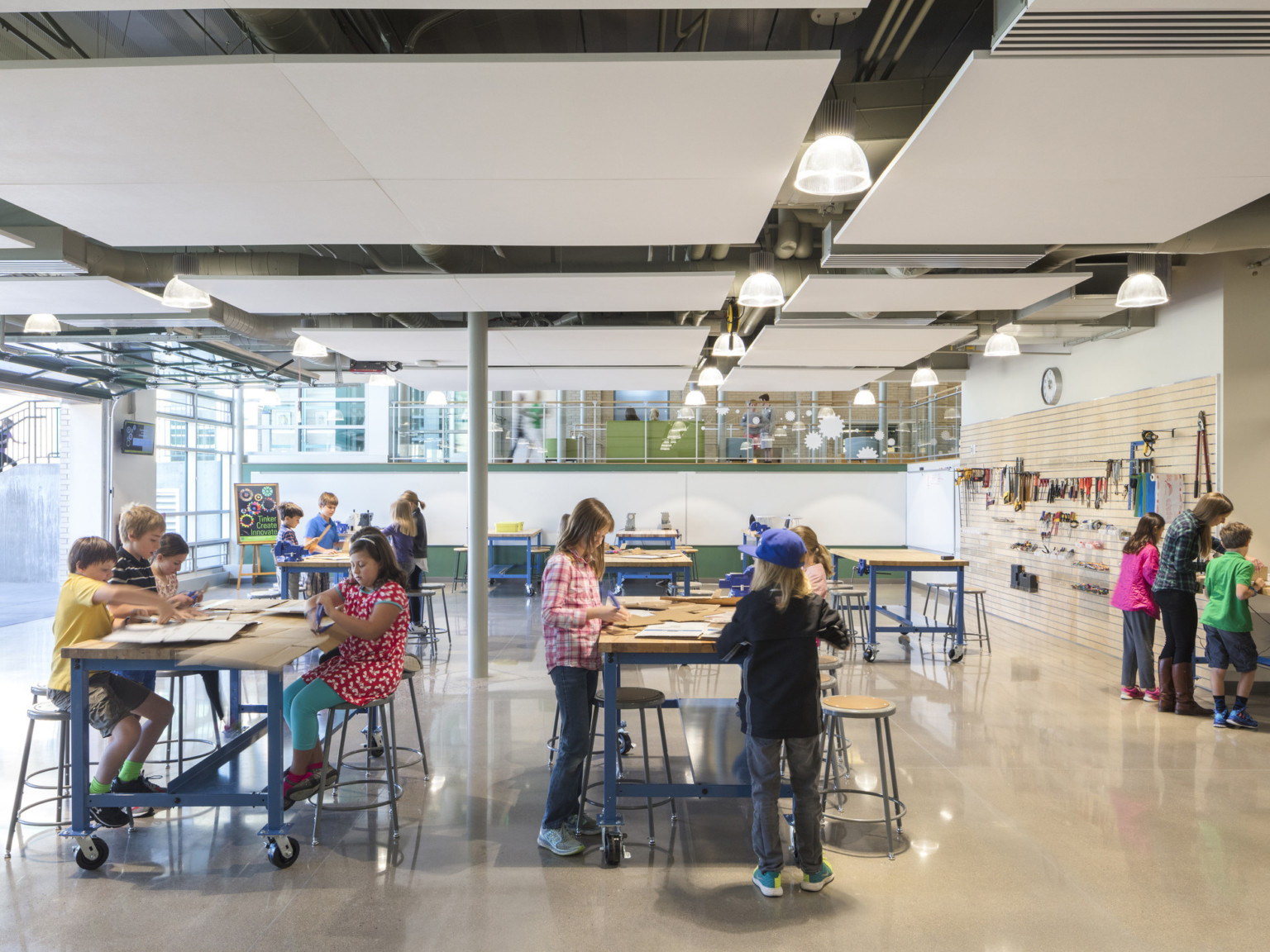 pendant lighting between suspended acoustic tiles in kids activity area with work tables backless stools and concrete floor