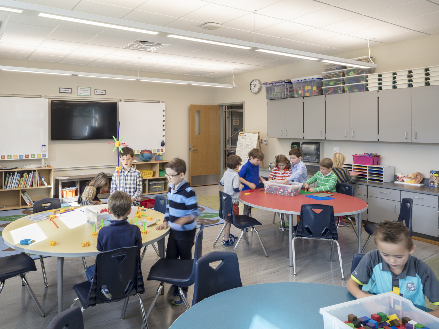 children's classroom with acoustic tile ceiling, suspended lighting gray storage shelves and red yellow and blue round tables