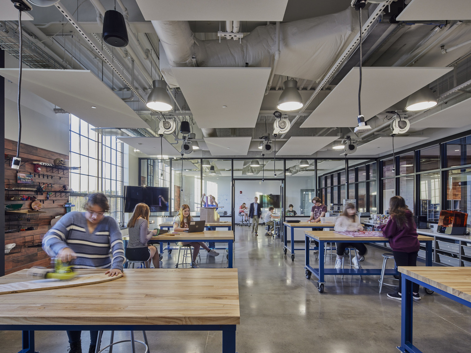 students wood working in an open classroom with windows to interior atrium and white acoustic panels over ceiling