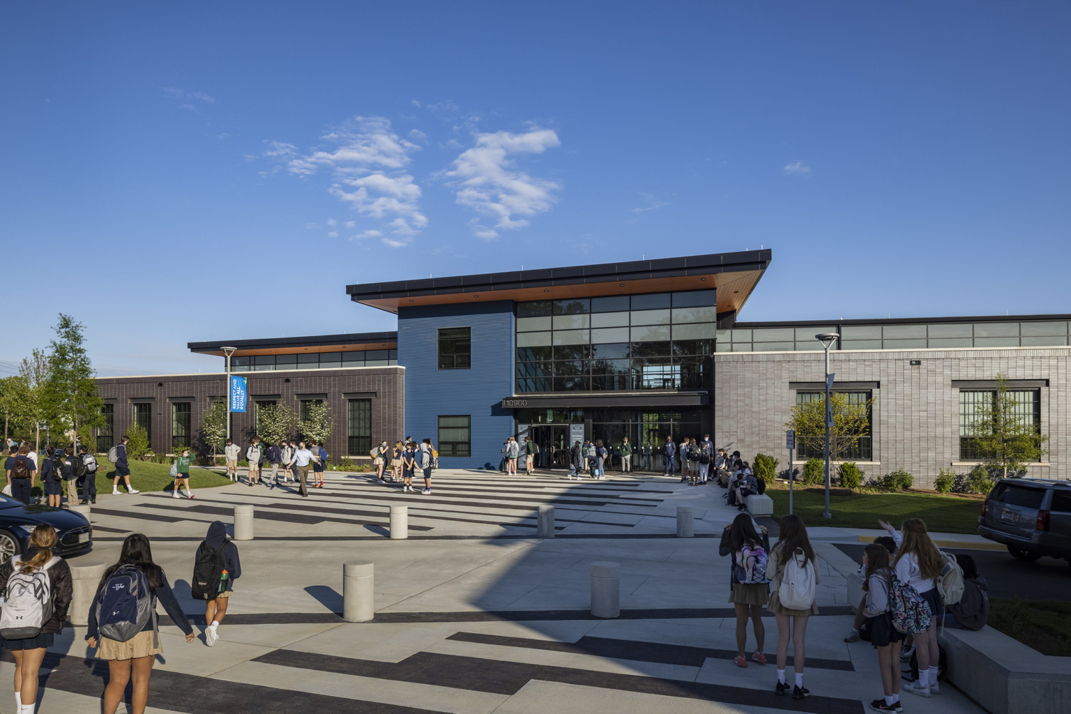 students walking up to a modern school with a double-height glass atrium flanked by a modern brick façade