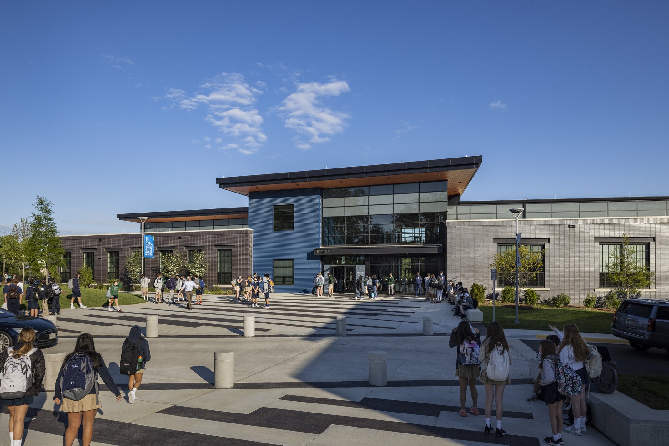 students walking up to a modern school with a double-height glass atrium flanked by a modern brick façade