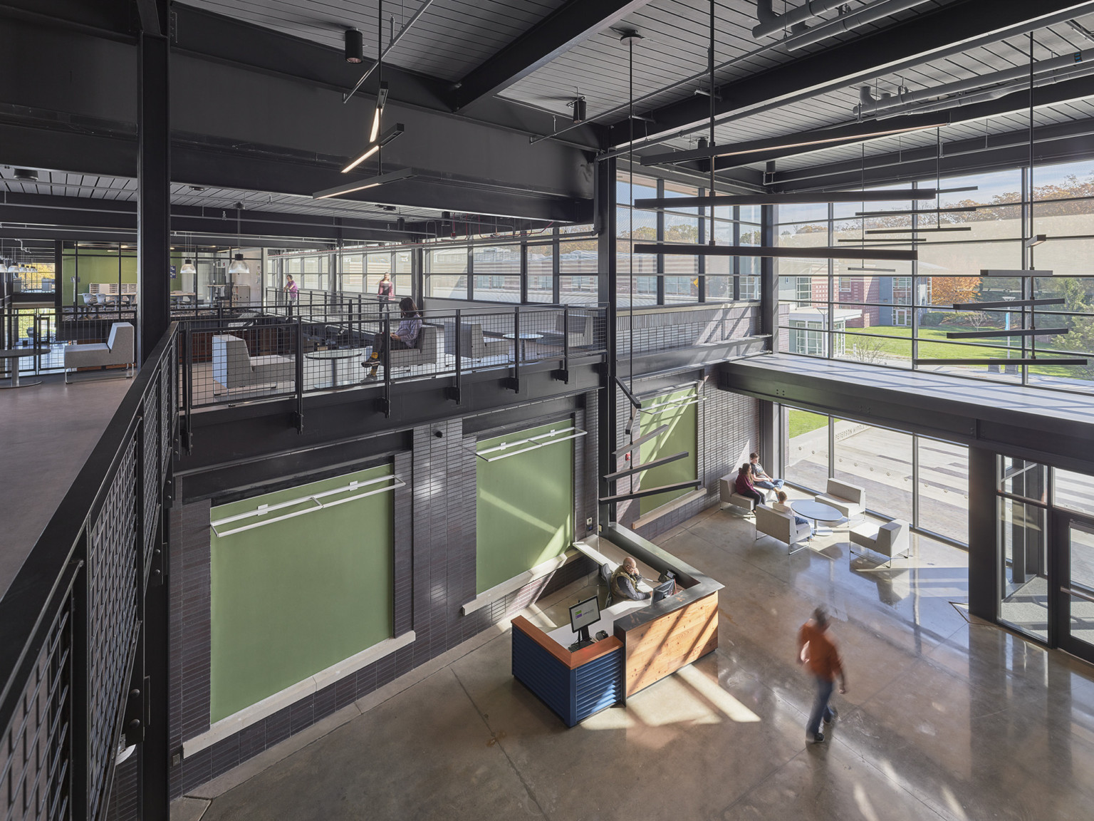 reception desk in a double height hallway with a mezzanine above with black metal railings and bright green wall color