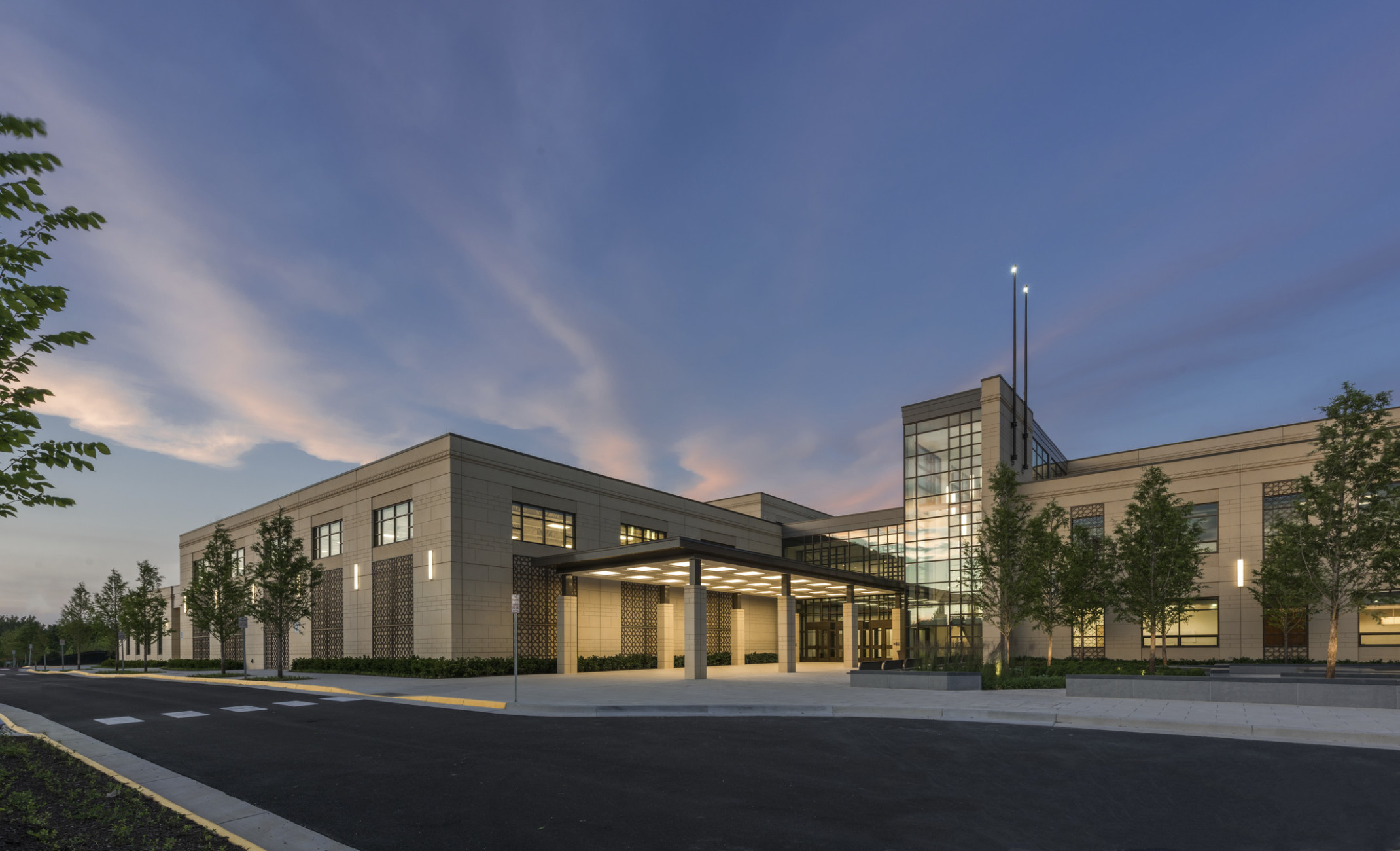 evening view of a precast concrete façade with an illuminated canopy entrance, a double-height glass atrium, and middle eastern inspired façade design