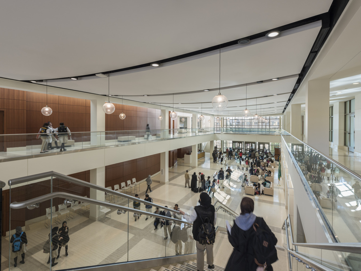 central atrium at a school with a large stair connecting the upper and lower floors, wood panel walls and white hallways