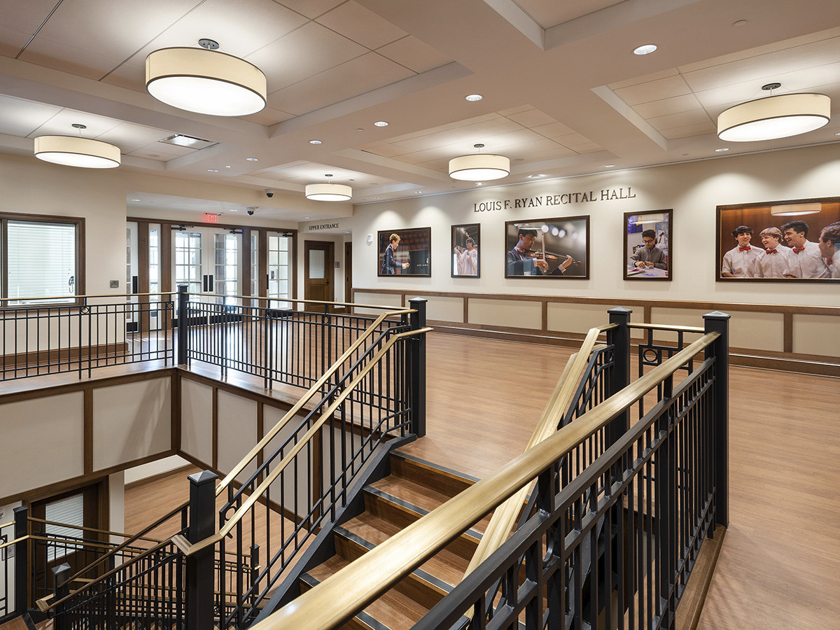 black wrought iron stair with brass hand rail leading to wooden floor landing with theatrical photos and pendant lights