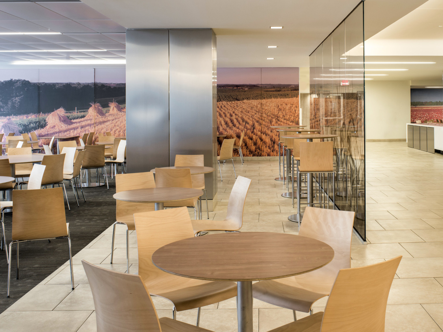 Flexible seating area with wood chairs, tables, and stools. A mural on the back wall shows a field of grain