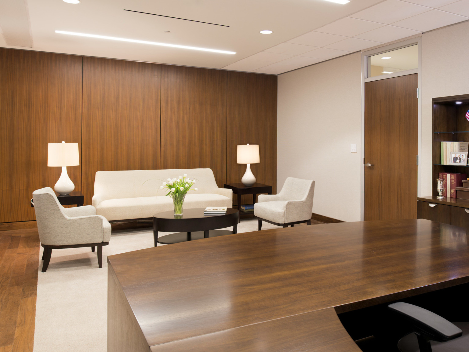 Wood desk, door, floor, and rear accent wall. Right wall and ceiling are white. White couch and chairs with coffee table mid