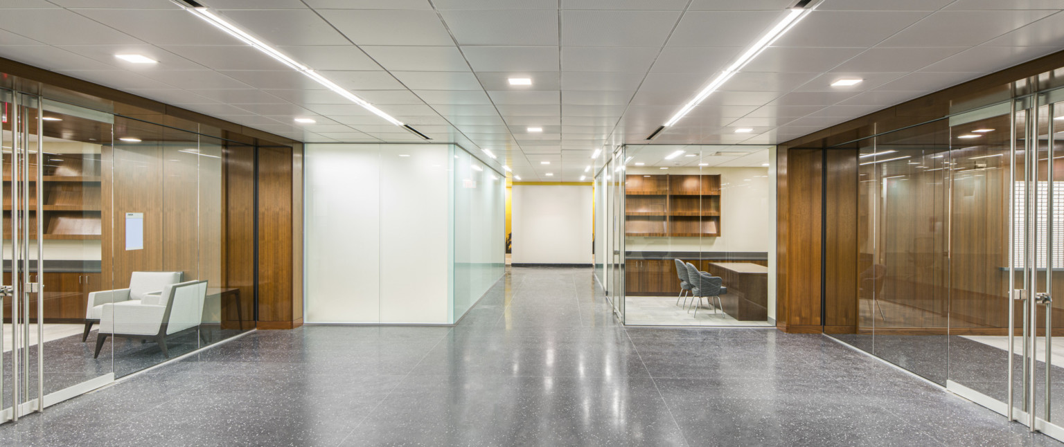 Interior hallway in the GSA Harry S. Truman Federal building with white walls and wood details. Glass offices to either side