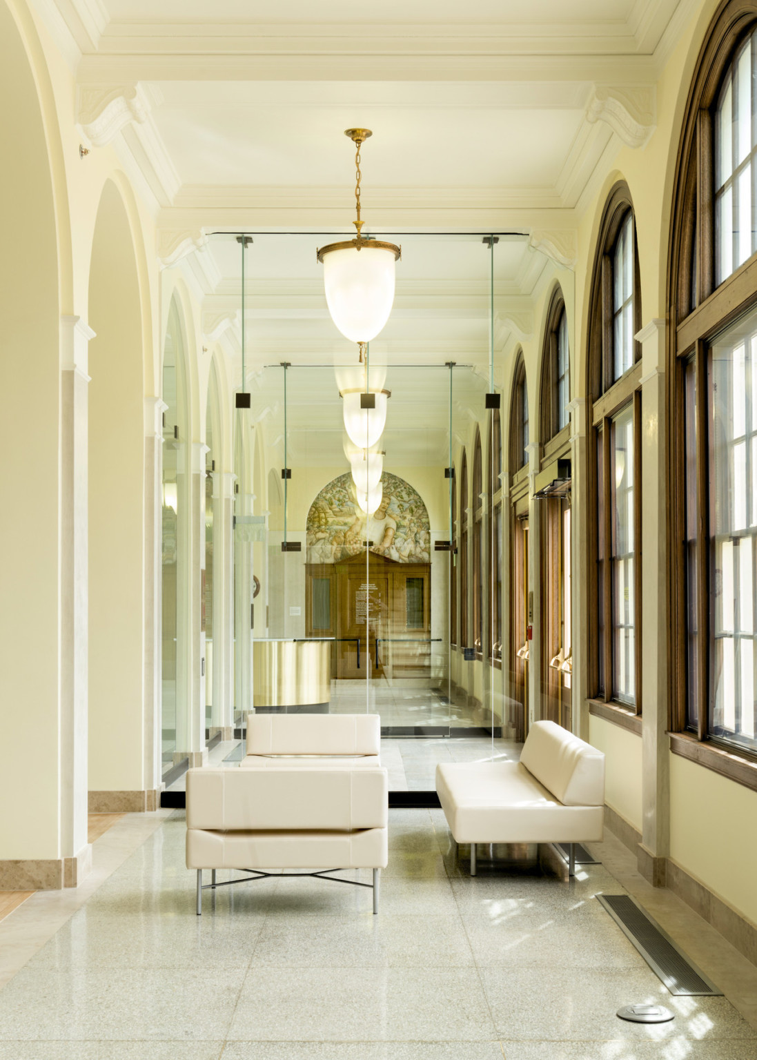 View of hallway's opposite direction, gold desk reflected in mirror at end of hallway with arched windows and hanging light