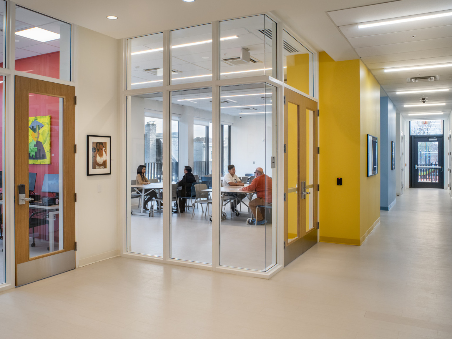 Colorful hallway with transparent glass wall room at center where pairs sit at tables