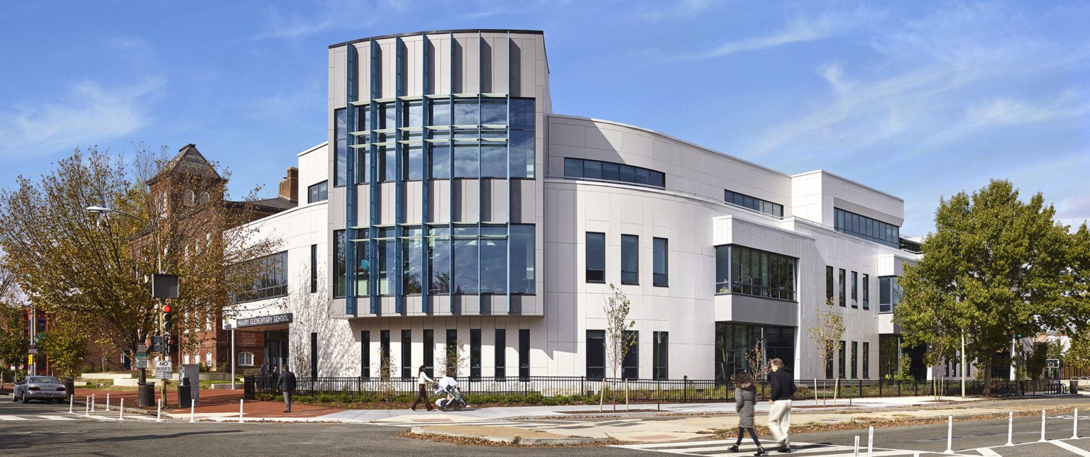 Rounded corner of white 3 story building with overhanging facade on 2nd and 3rd floor corner with large paneled sunscreens