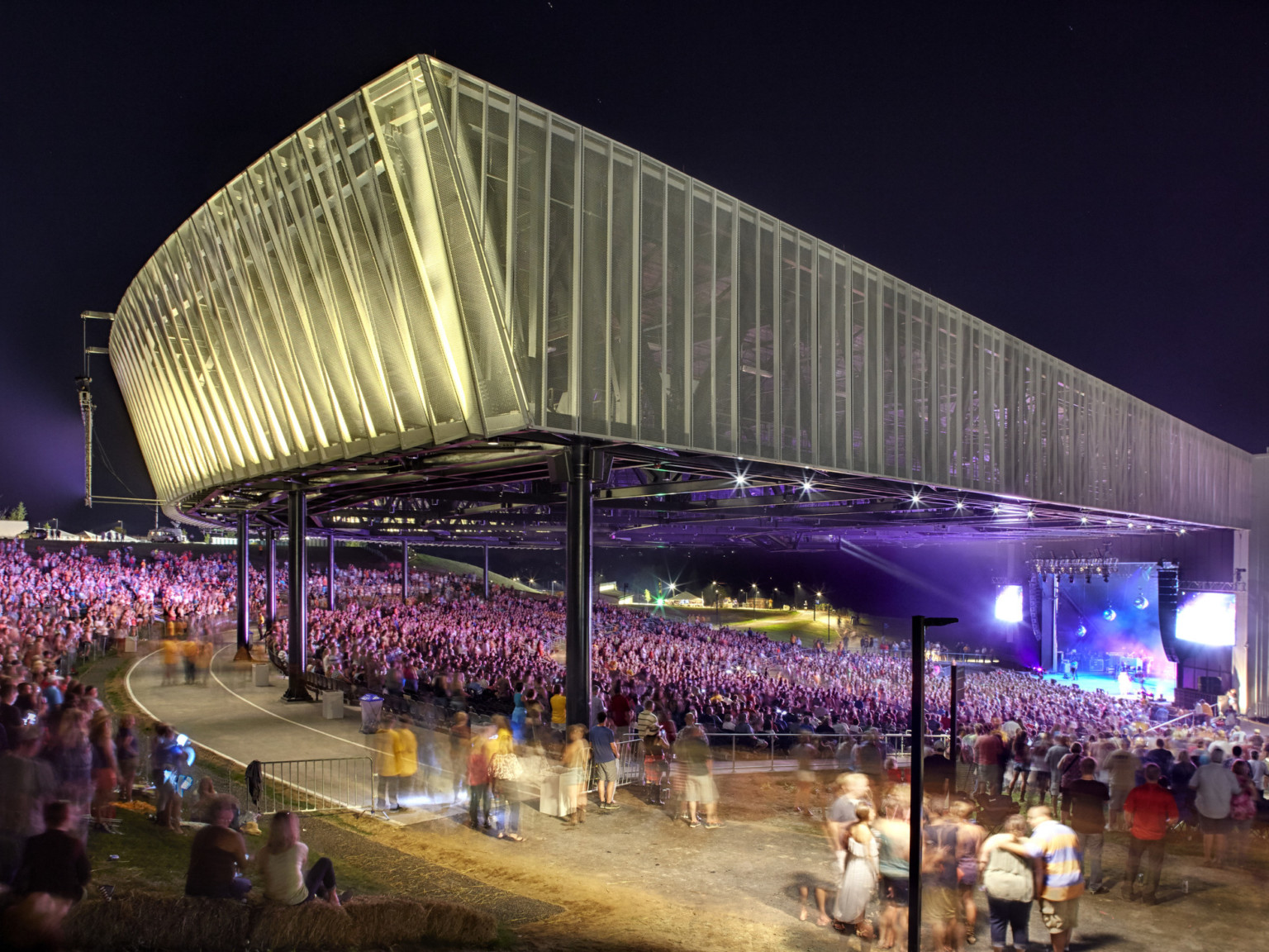 Corner view of crowd in partially covered St. Joseph Health Amphitheater at Lakeview at night while band performers on stage