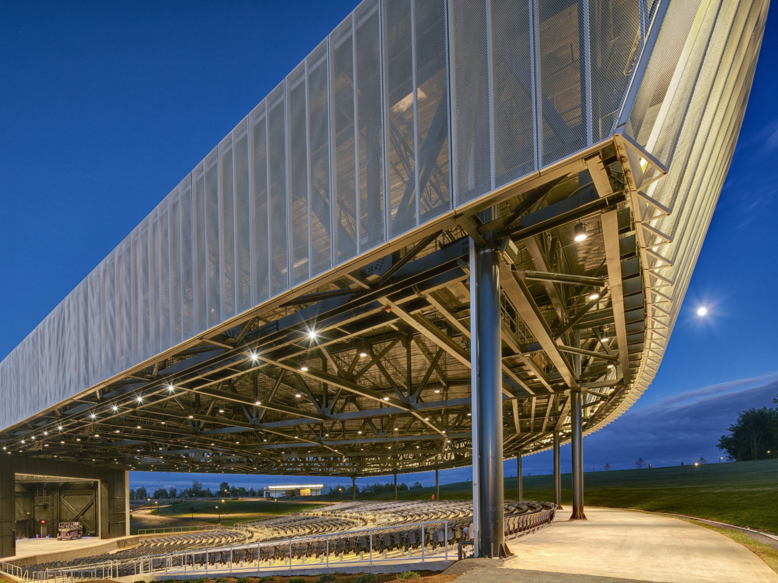 Amphitheater with lights in rafters viewed from front corner facing stage, showing ridges along fascia front