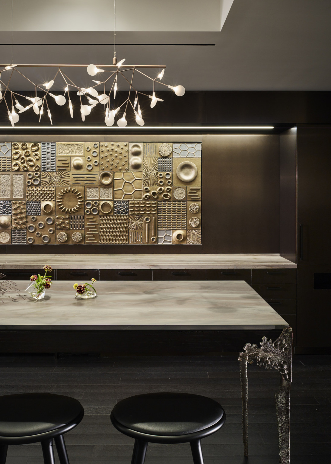 High top table in front of dark wood wall with illuminated recessed counter. Recessed ceiling detail with sculptural light