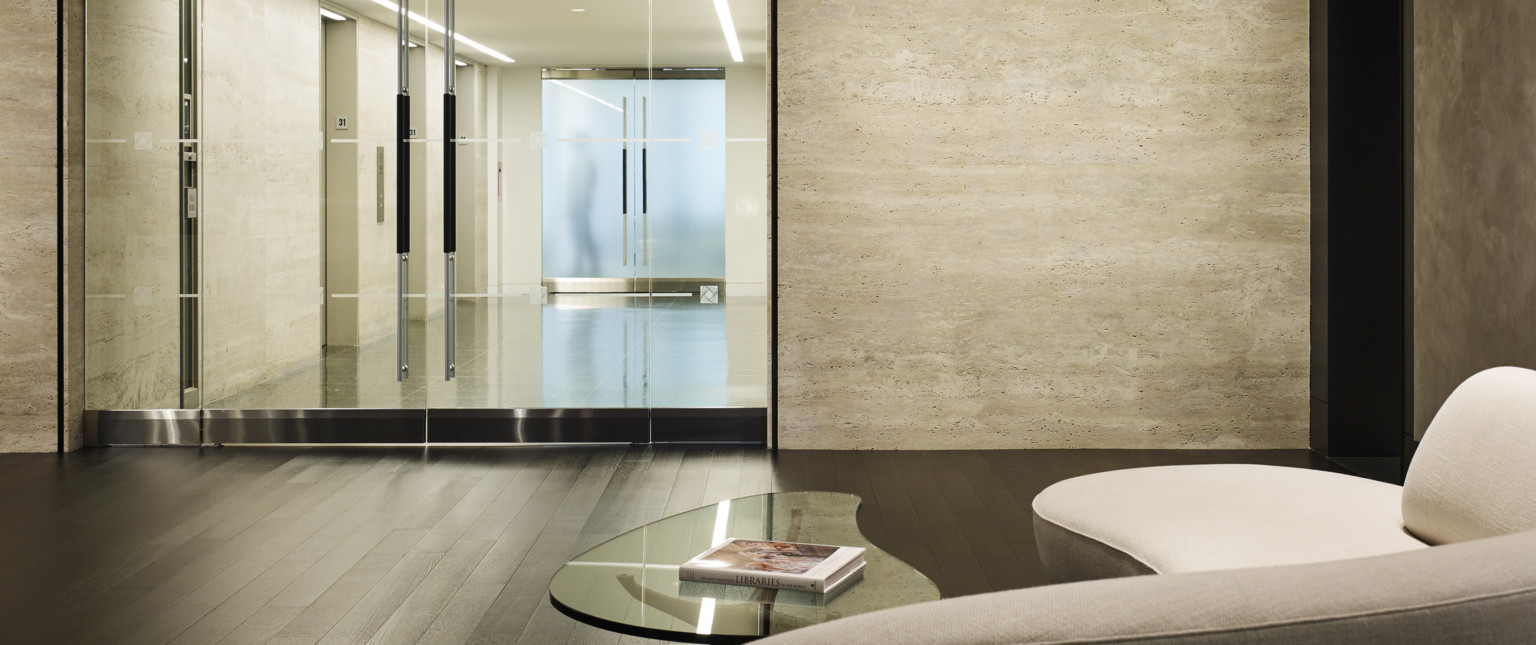 Seating and coffee table in front on glass double doors looking to elevator hallway with light colored walls