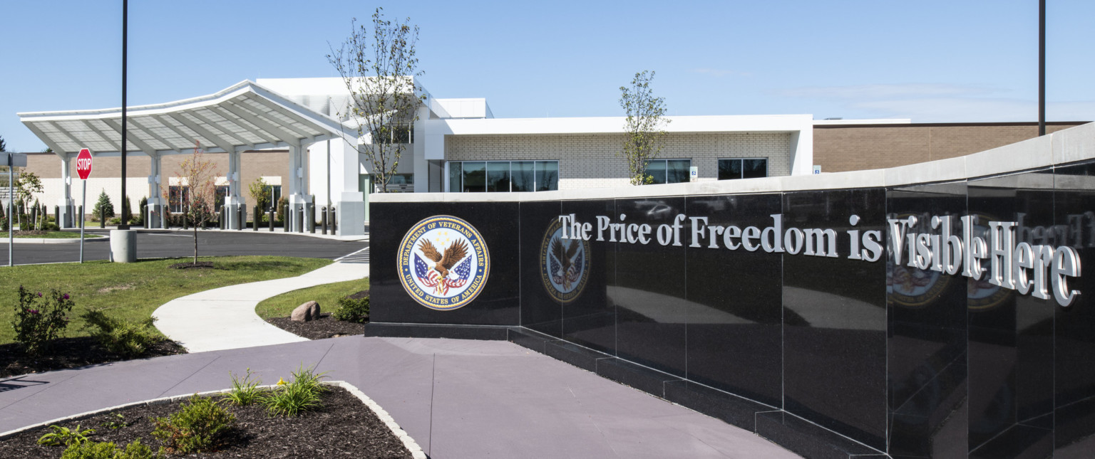 Partial view of black sign with Department of Veteran Affairs logo in front of building entry with angular awning