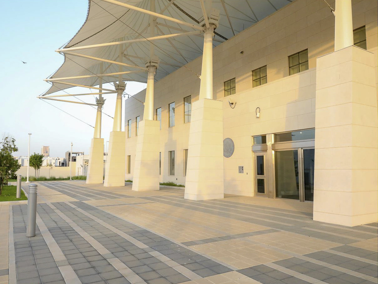 White stone building with stone based pillars and metal upper and trusses supporting awning. Tiled entry plaza, front