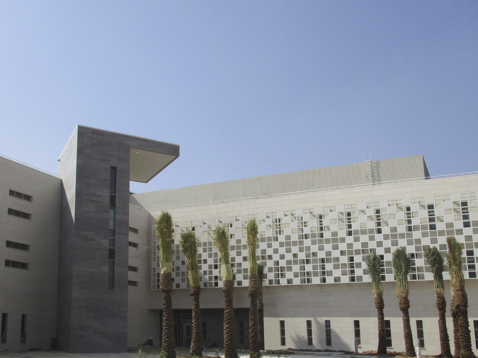 White building corner with grey outcrop with overhang for shade. Right side has tiled translucent screen on upper floors