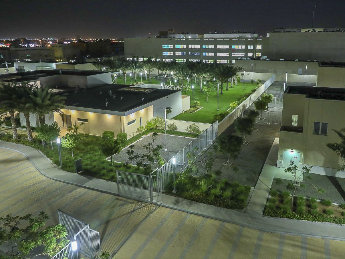 View from above of square buildings in neutral colors surrounded by greenery. Fence divider down the center.