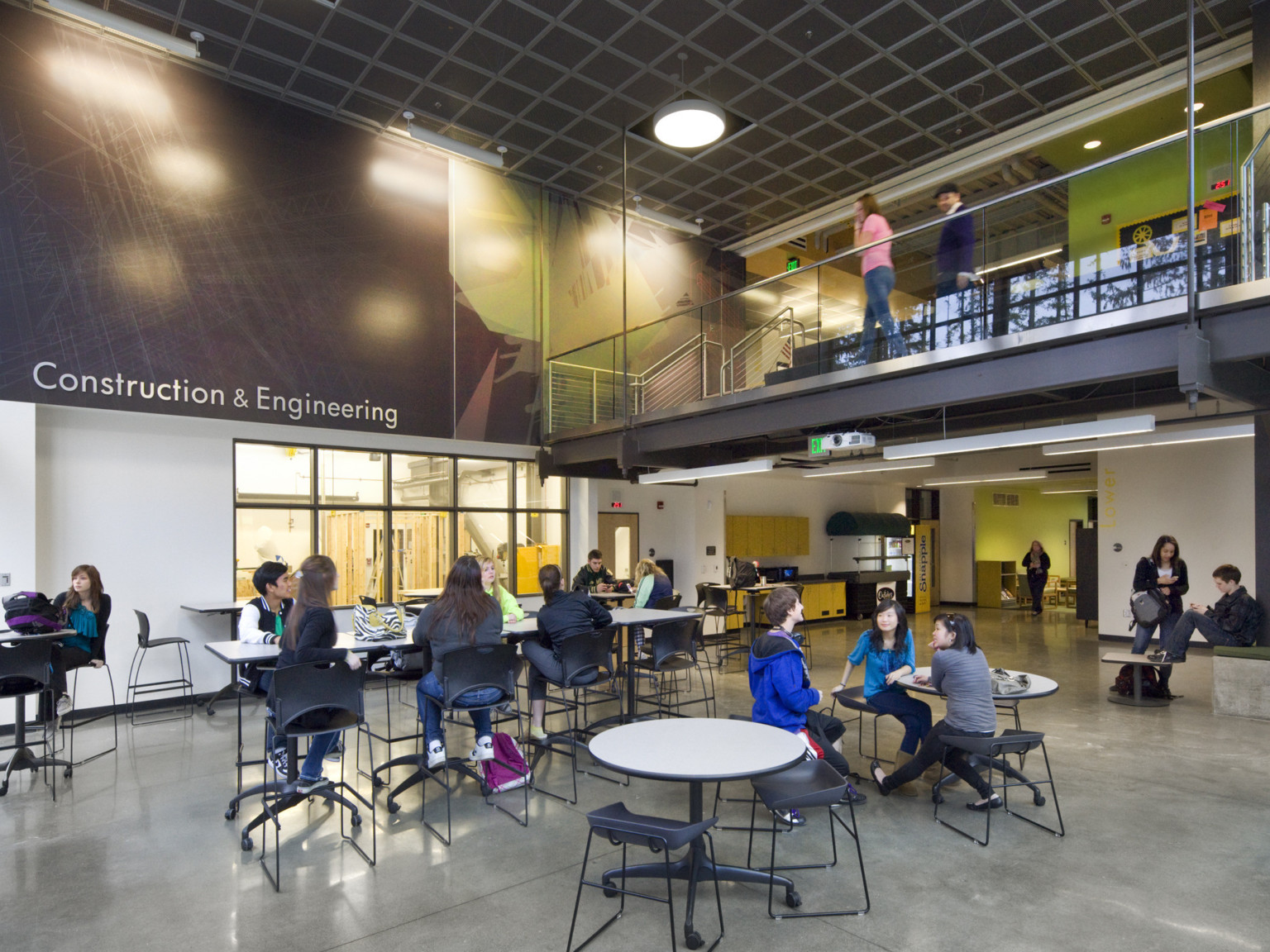 Flexible seating in double height room with walkway above right. Green and brown mural with Construction and Engineering sign