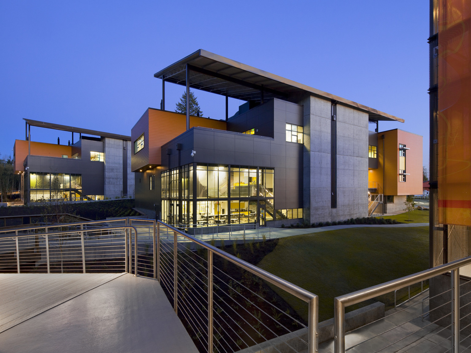 Layered building with double height glass corners illuminated from within. Angled roof panels supported by exposed beams