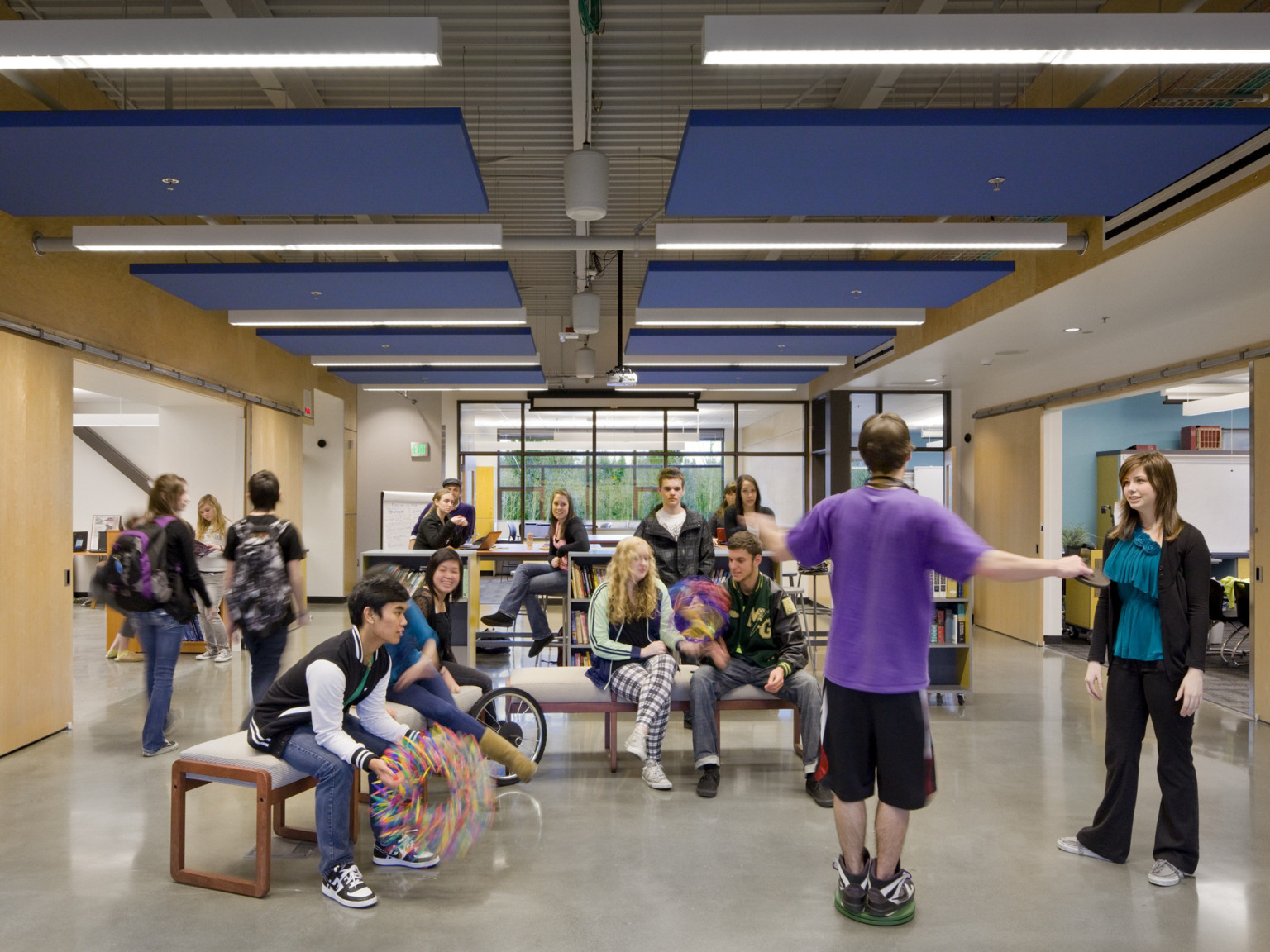 Benches in white hallway between classrooms with wood sliding double doors opened. Blue panel drop ceiling details and lights