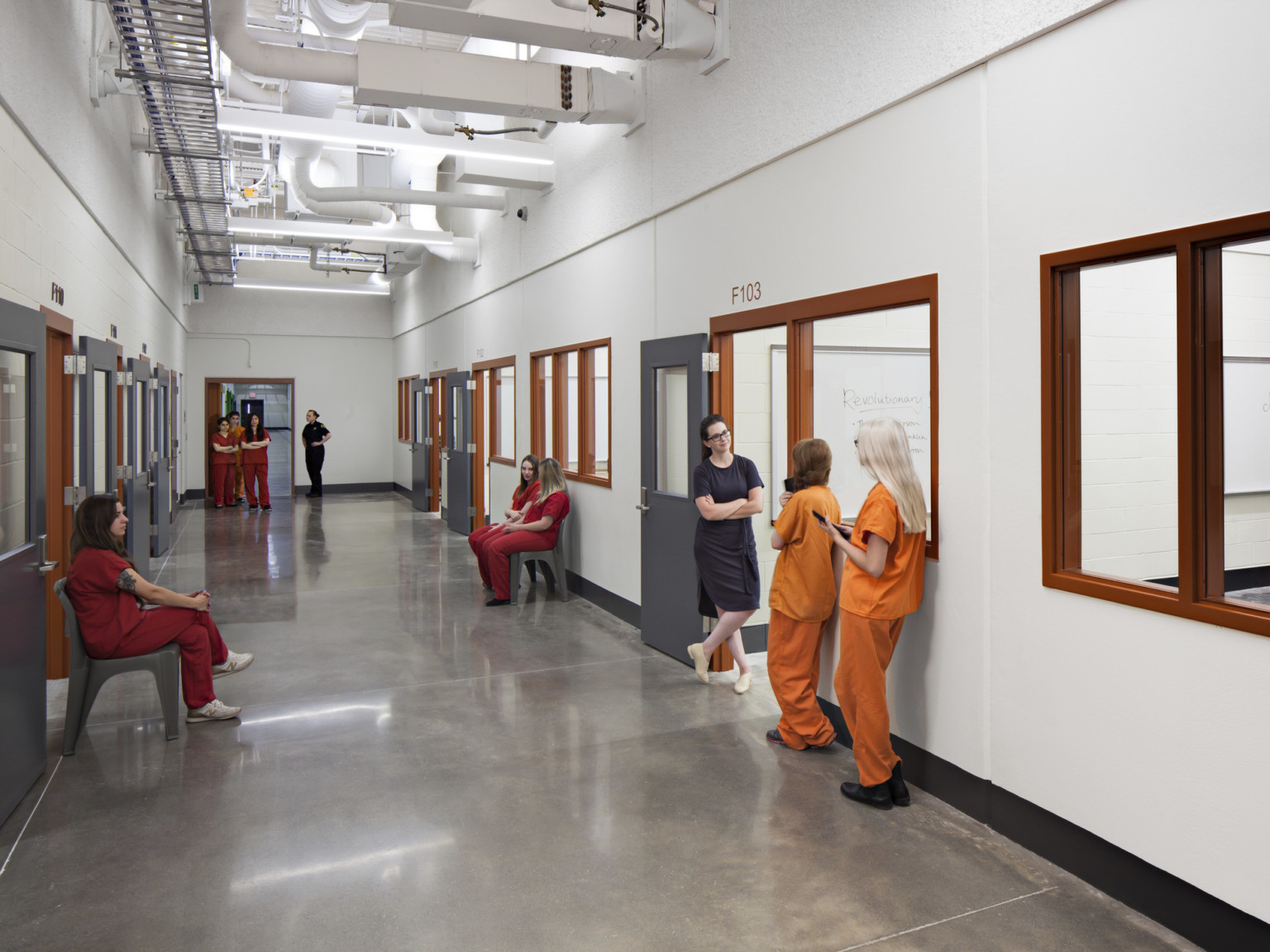 White hallway with grey doors and orange window frames. Exposed ductwork and beams above grey tile flooring