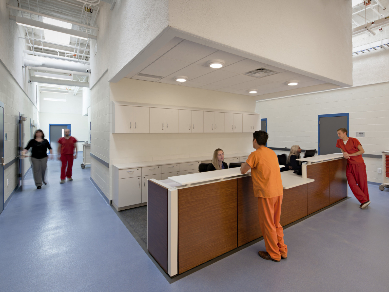 A large white column with recessed section. Cabinets line the area's back wall behind a wood paneled desk with white counter