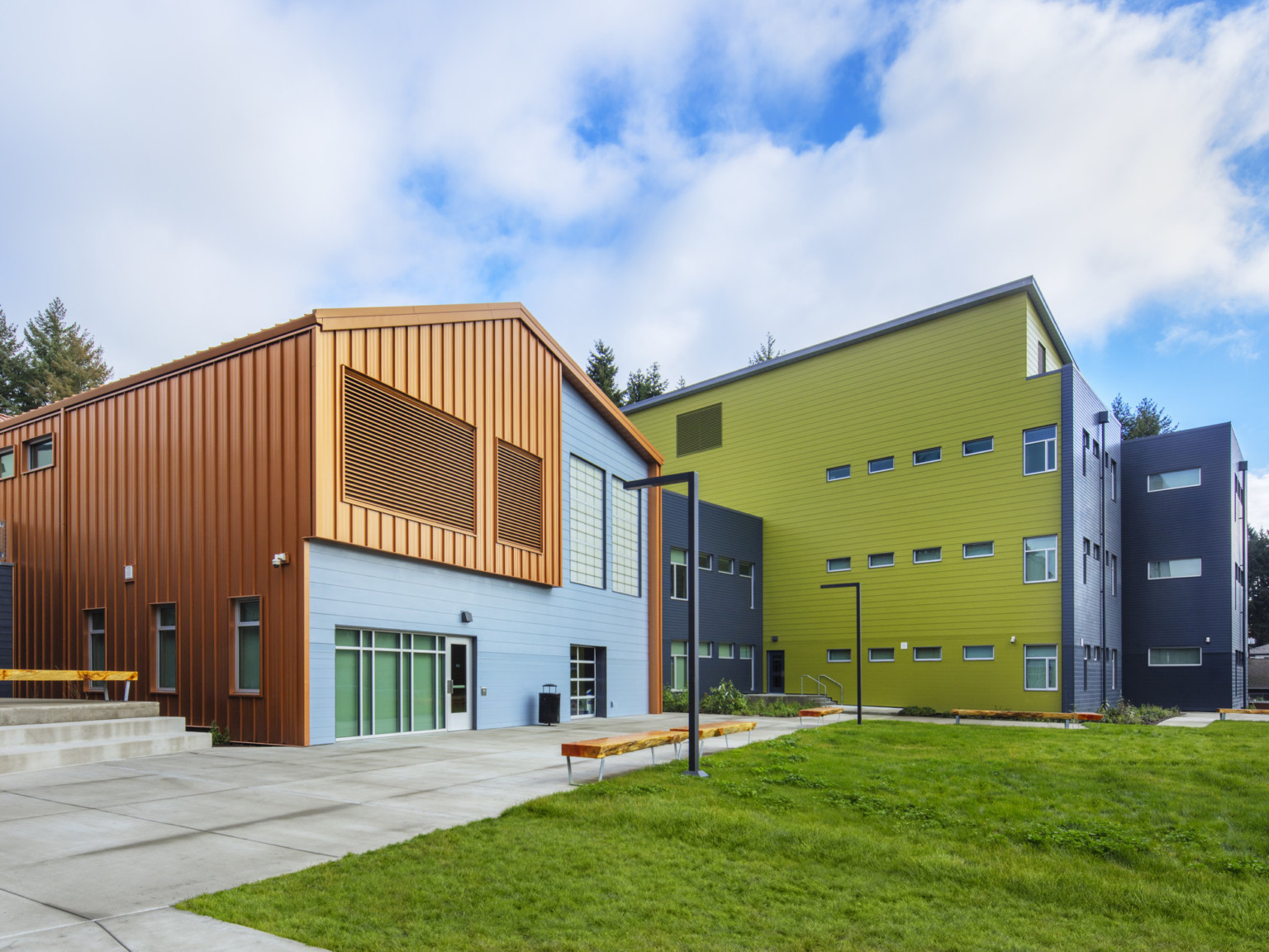 Back exterior of building in front of lawn. Orange and blue colorblock building front, connecting to a black and yellow site