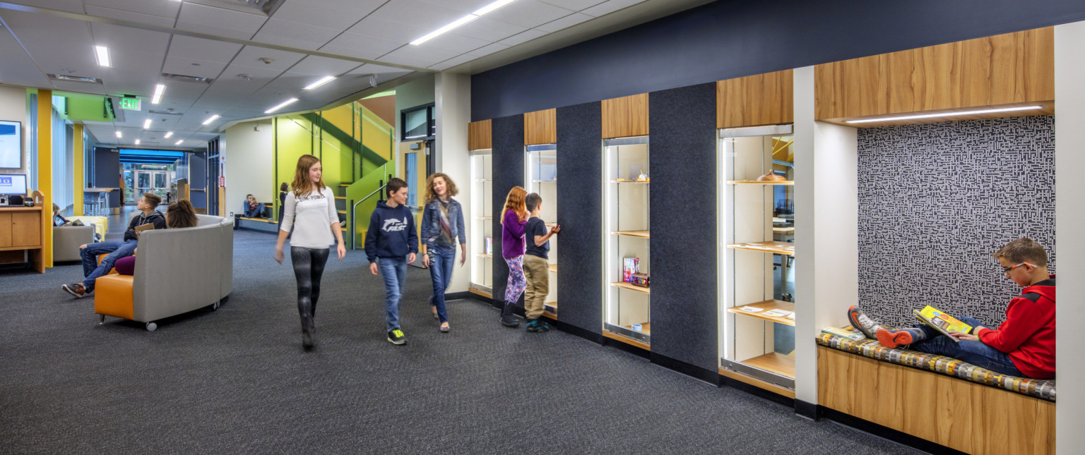 Hallway with blue wall with wood accents, recessed seating and display shelves. Hall leads to seating and green stairwell