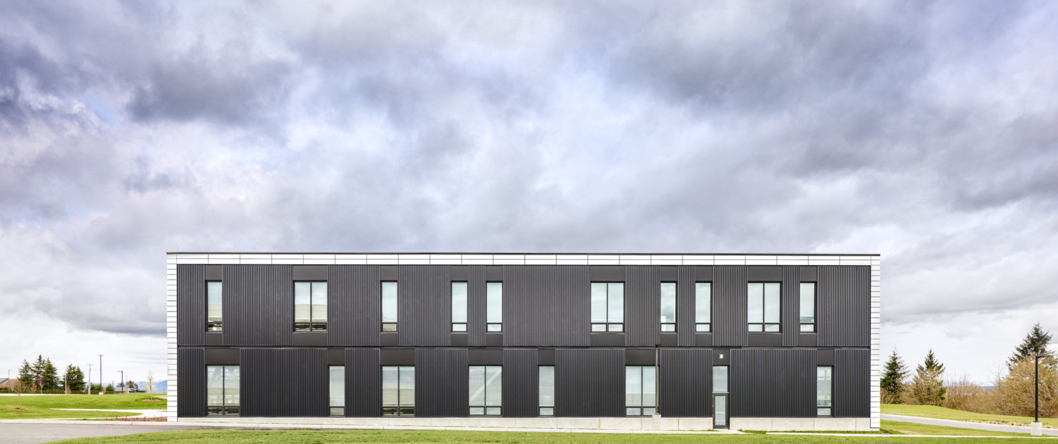 Exterior view of back of building. Black paneling with white tiles around top and side. The building is surround by grass