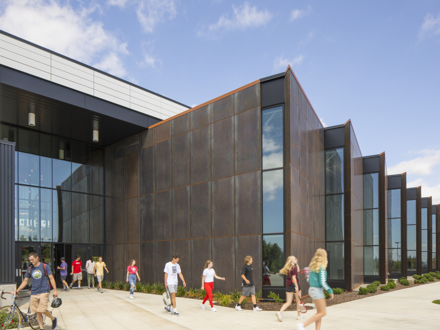 Front entrance of building looking towards brown stepped angled building extensions with strips on windows at end