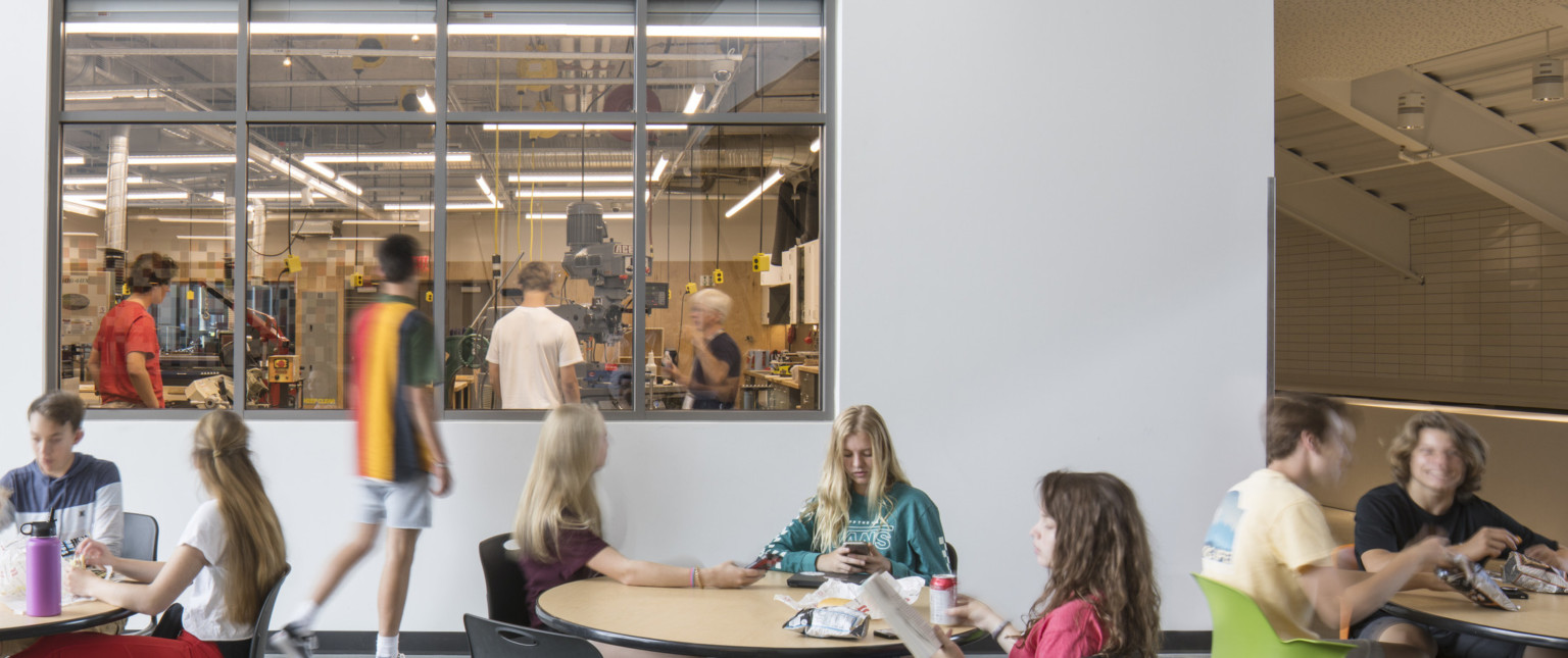 Dining area with window in white wall looking into classroom