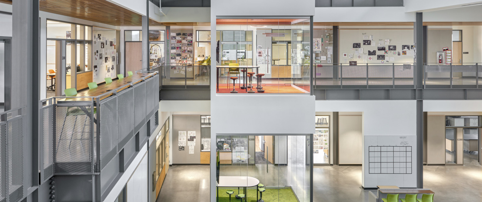 Viewed of atrium from the top of the stairs facing learning pods. 2nd floor hallway has wall collages and high top table